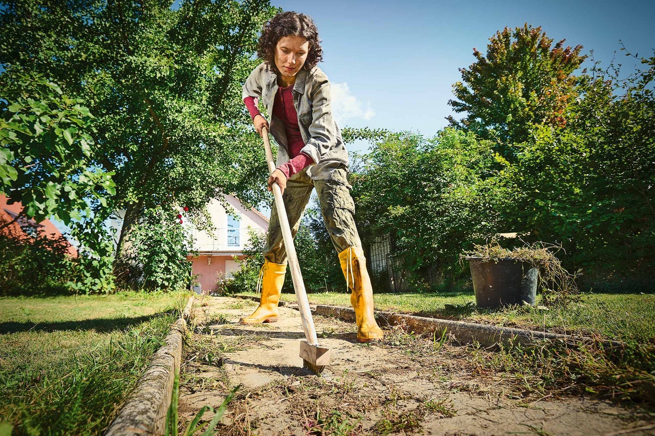Frau entfernt Unkraut mit einer Fugenbürste im Garten.