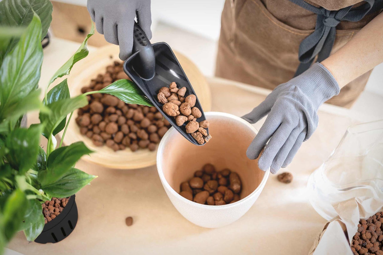Eine Person mit Gartenhandschuhen füllt Blähton mit einer Schaufel in eine Schale.