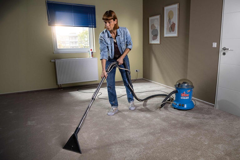 Frau reinigt Teppich mit einem Teppichreinigungsgerät in einem Zimmer.