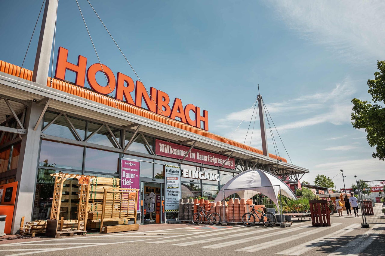  Außenansicht eines Hornbach Baumarktes mit Eingangsbereich und verschiedenen Warenangeboten. 