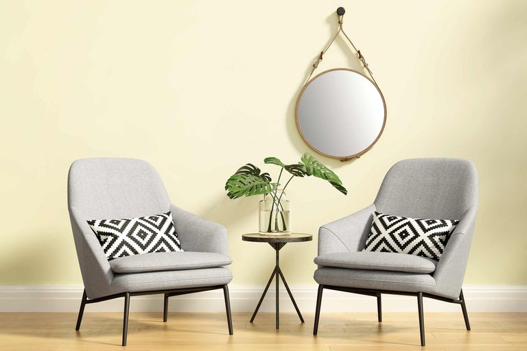 Zwei Sessel mit Kissen, ein Tisch mit Pflanze und ein runder Spiegel an der Wand.