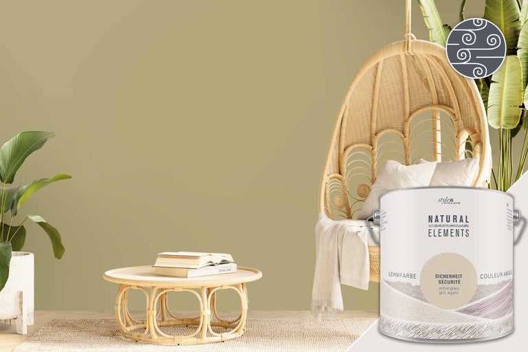 Raumszene mit einem Eimer Lehmfarbe, einem Rattansessel und einem Tisch