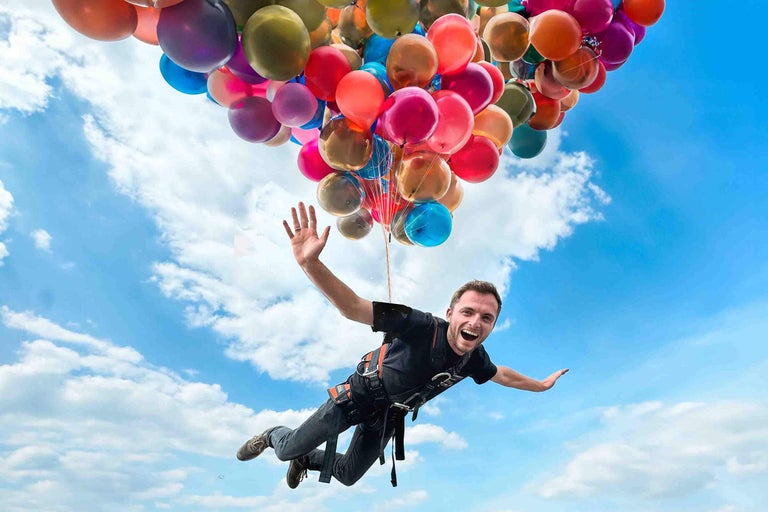 Mann schwebt mit vielen Ballons am Himmel