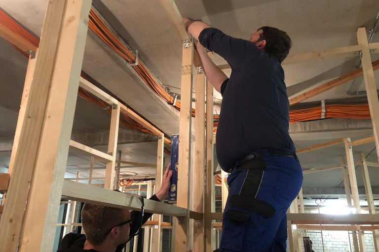 Zwei Handwerker arbeiten am Holzrahmenbau mit Wasserwaage und Kabeln an der Decke.
