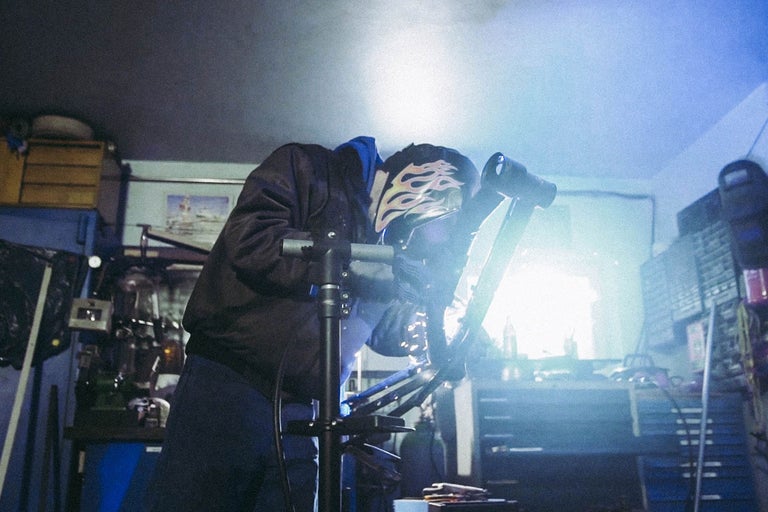 Person schweißt Metall mit Schweißhelm in Werkstatt