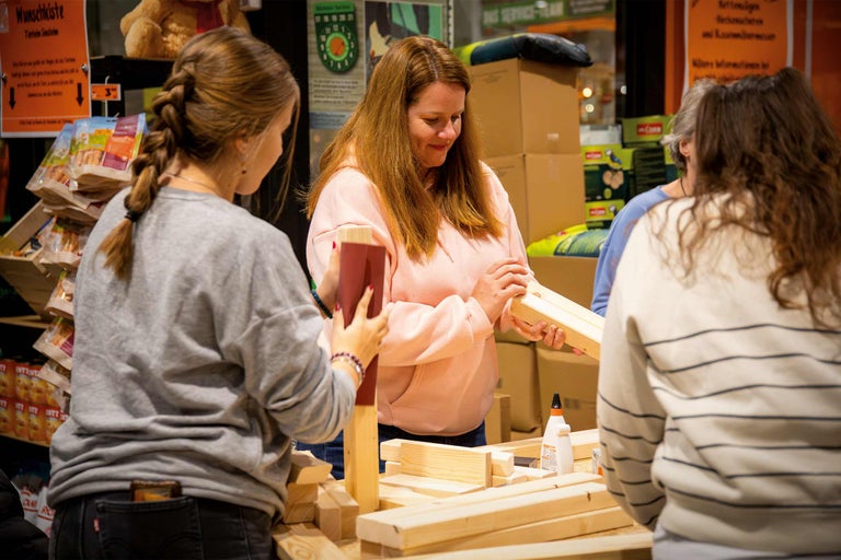Personen bauen mit Holzstücken und Klebstoff eine Wunschkiste.