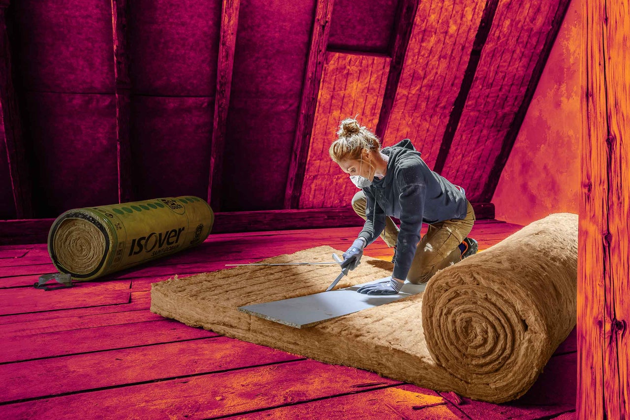 Frau schneidet Dämmwolle im Dachgeschoss mit Isover Dämmstoffrolle.
