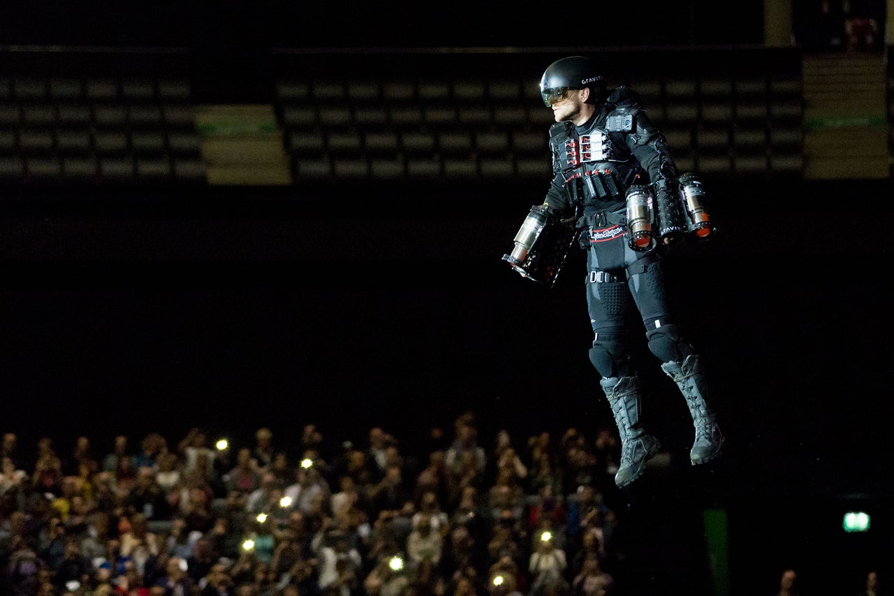 Eine Person, die ein Jetpack trägt, schwebt vor einer Menschenmenge.