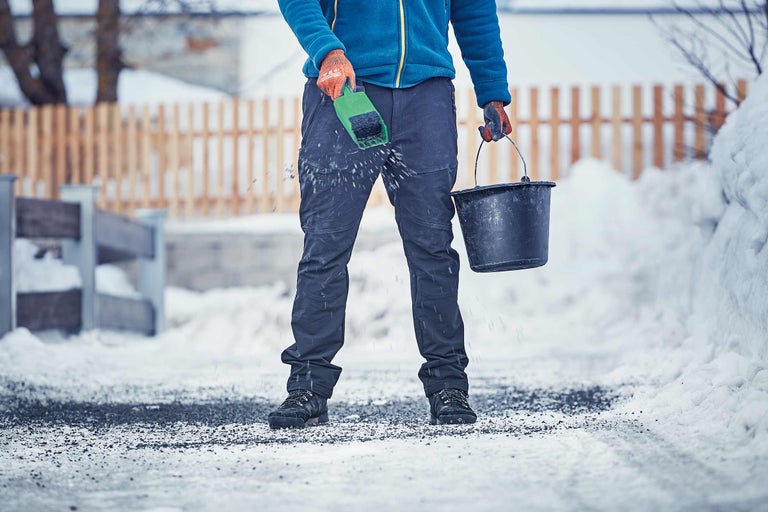 Mann streut Streugut mit einer Schaufel im Winter