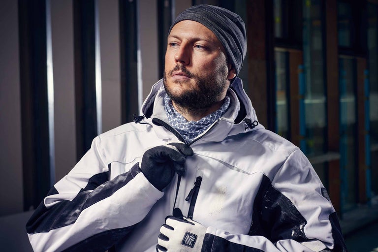 Mann mit Mütze, Multifunktionstuch, Arbeitshandschuhen und Arbeitsjacke