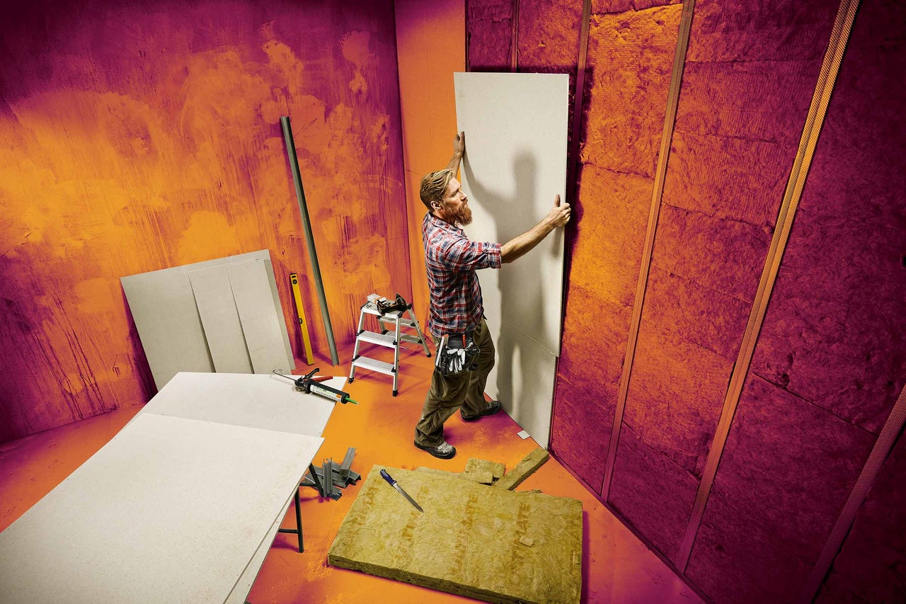Mann montiert Trockenbauwand mit Dämmmaterial und Metallprofilen in einem Raum.