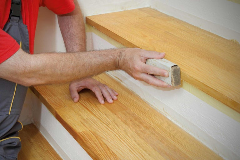 Handwerker bearbeitet Holztreppe mit Schleifklotz