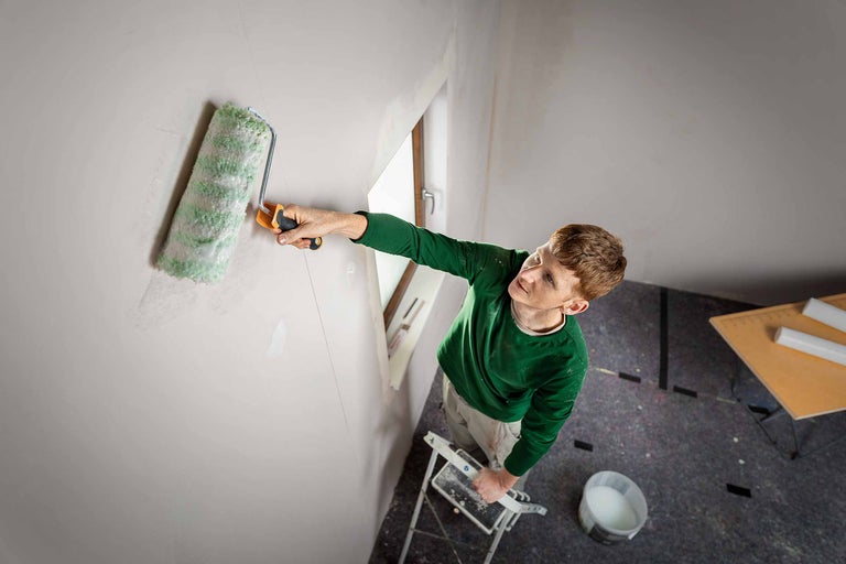 Mann streicht Wand mit Farbroller, stehend auf Leiter