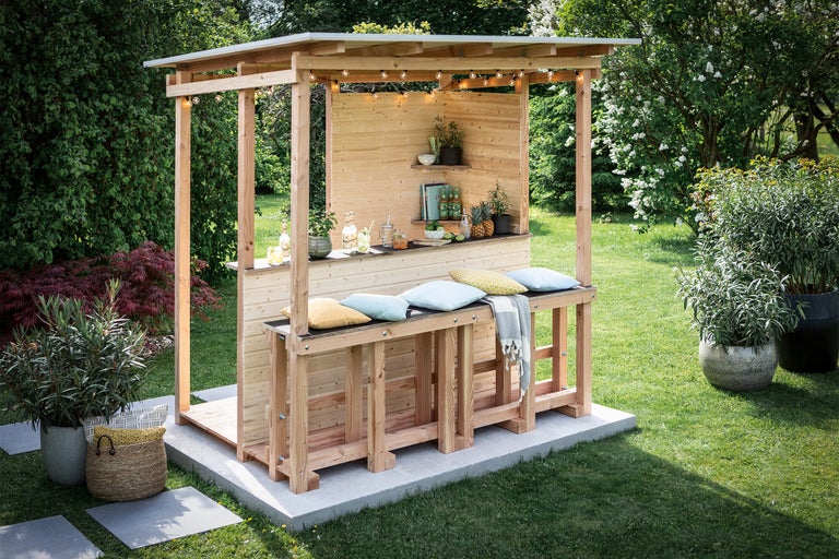 Holzgartenbar mit Getränken und Dekoration in einem grünen Garten.