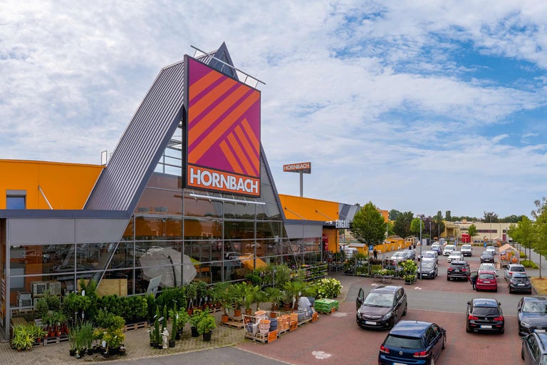 Außenansicht eines Hornbach Baumarktes mit Parkplatz und Pflanzen vor dem Eingang