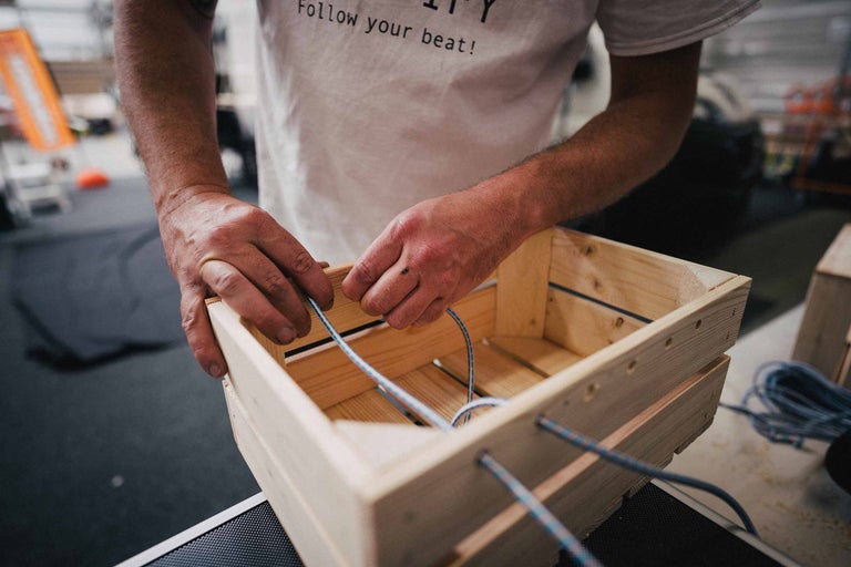 Mann fädelt eine Gummischnur in eine Holzkiste ein