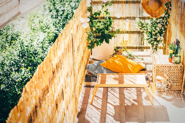 Balkon mit Bambuszaun, Pflanzen, Kissen, Tisch und geflochtenem Hocker