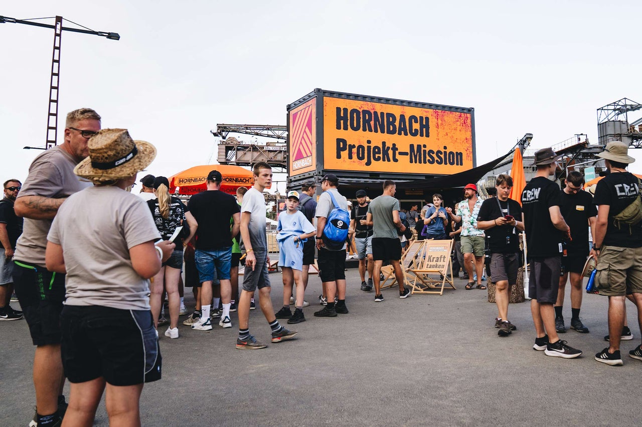 Eine Menschenmenge vor einem Hornbach Projekt-Mission Container auf einem Festivalgelände bei Tageslicht.