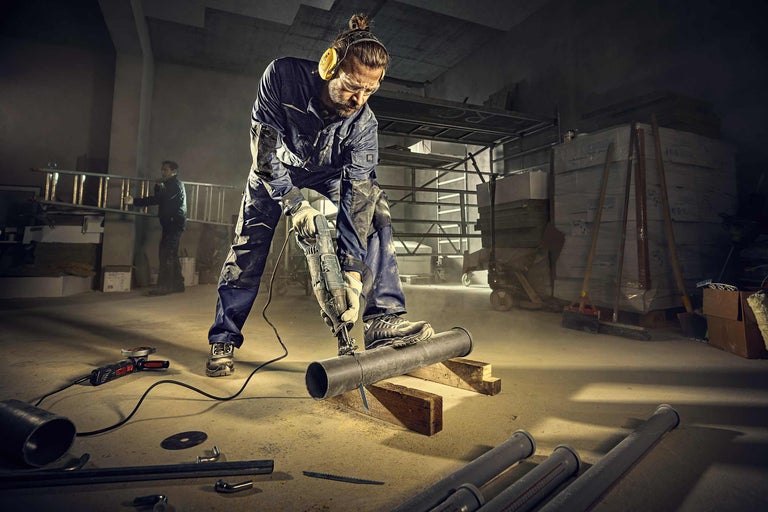 Handwerker sägt Rohr mit einer Säbelsäge in einer Werkstatt