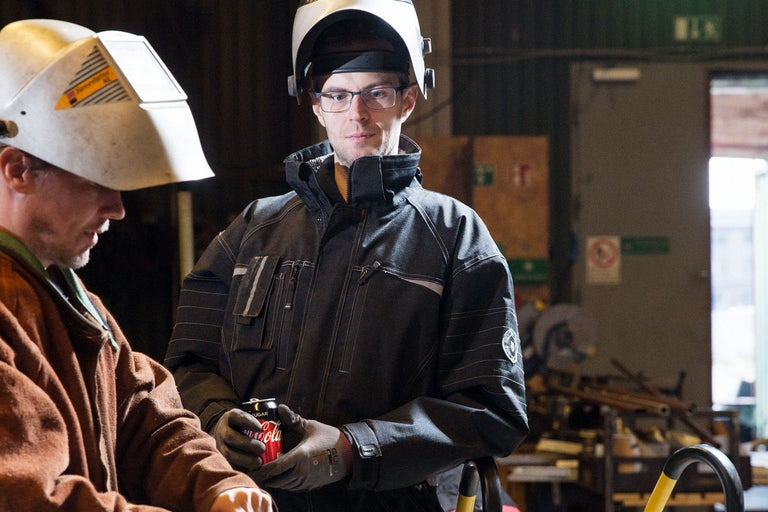 Zwei Handwerker mit Schutzhelmen und Arbeitskleidung in einer Werkstatt.