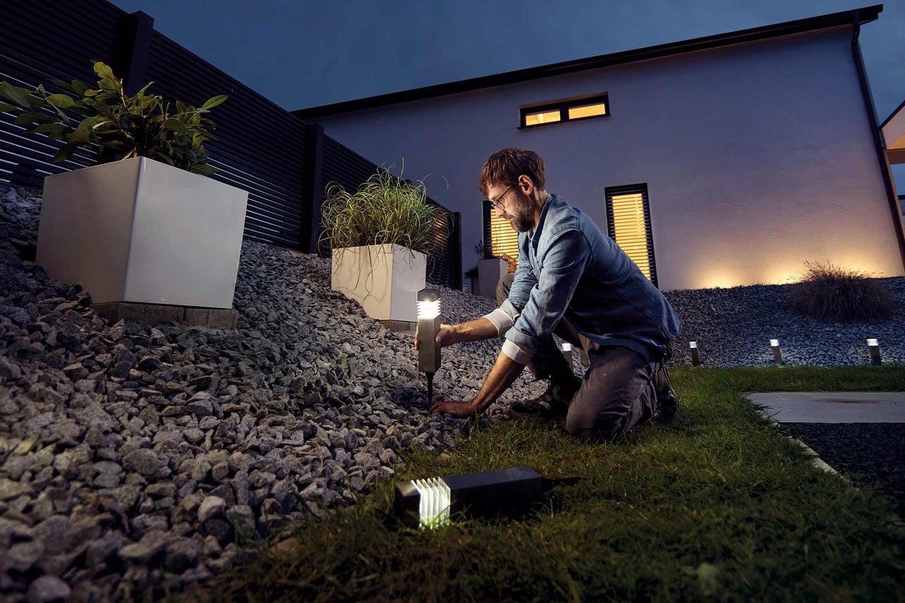 Ein Mann installiert eine Gartenleuchte in einem Garten mit Kies und Pflanzen