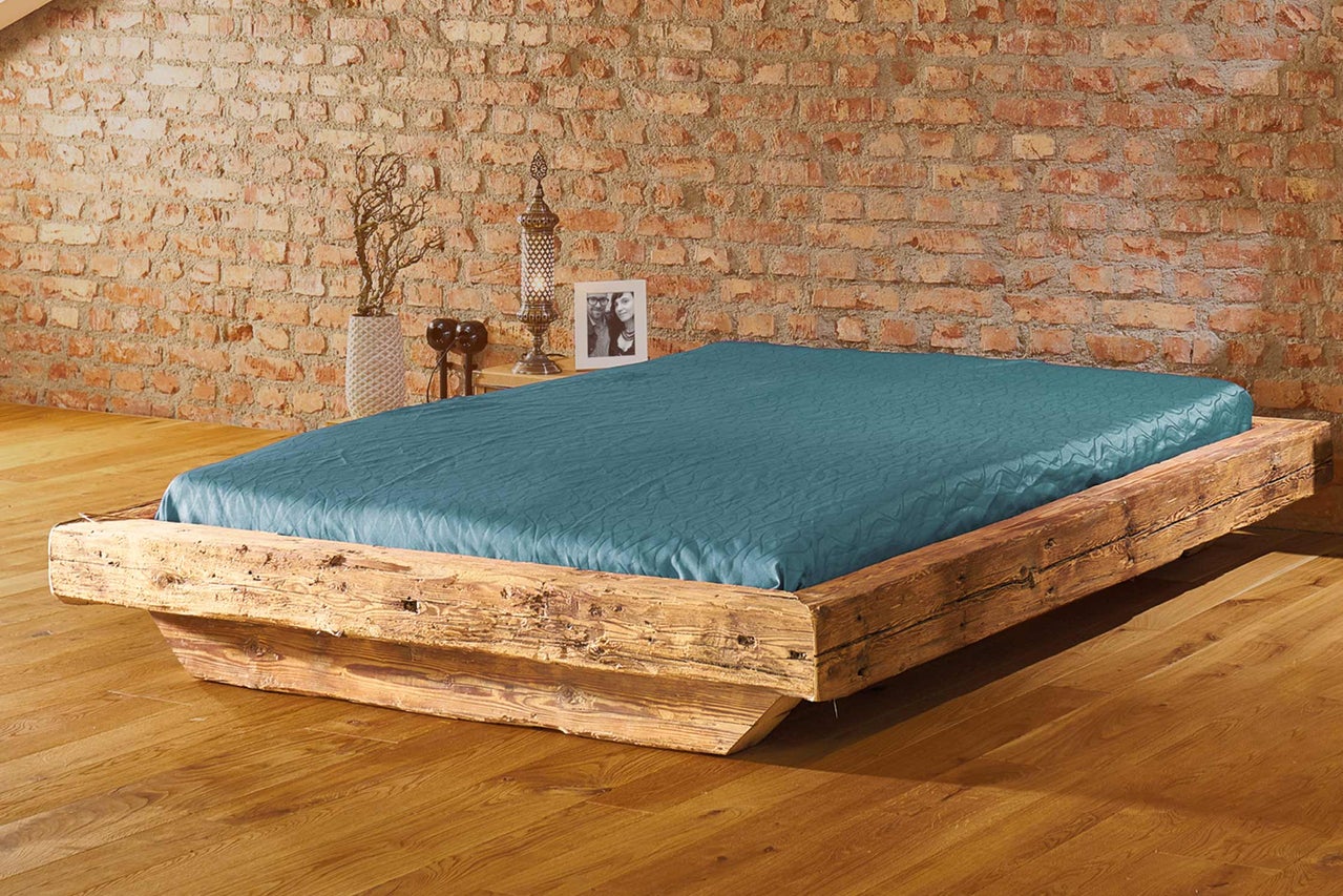 Bett mit Holzrahmen und blauem Bettbezug vor einer Ziegelwand