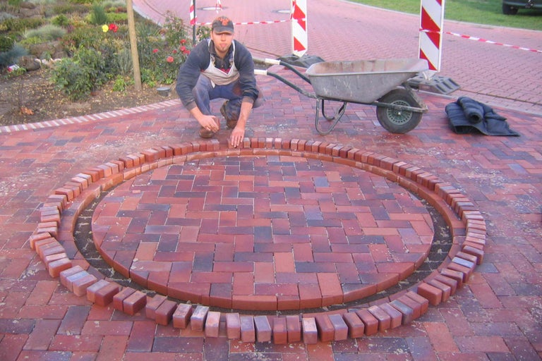 Mann verlegt Pflastersteine in einem kreisförmigen Muster für einen Gartenweg.