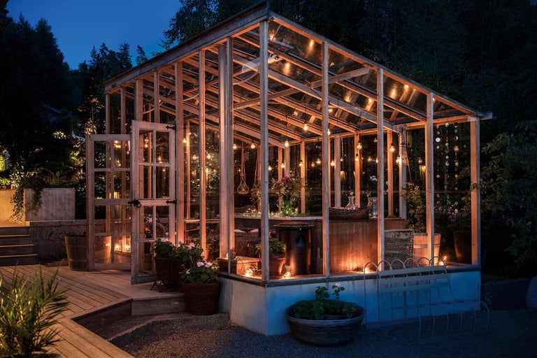 Illuminierte Gewächshausanlage mit Holzrahmen, Glaswänden und dekorativer Beleuchtung im Garten.