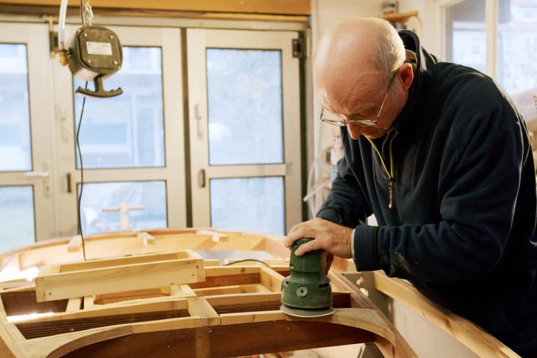 Ein Mann schleift Holz mit einem Exzenterschleifer in einer Werkstatt.