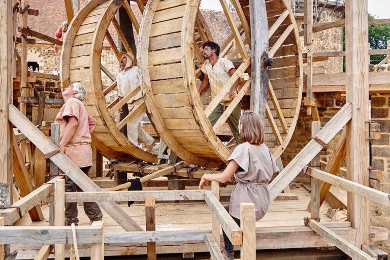 Szene mit Personen, die an einem großen Holzrad arbeiten