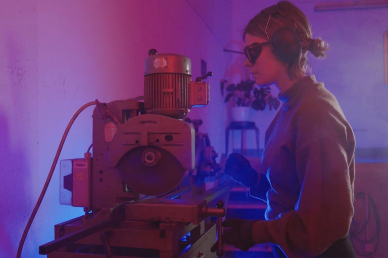 Frau bedient stationäre Metallkreissäge mit Schutzbrille und Gehörschutz