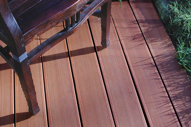 Terrassendielen aus Holz mit gerillter Oberfläche und einem Stuhlbein im Bild.