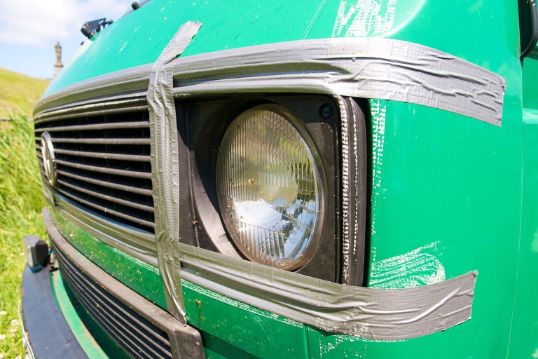 Nahaufnahme eines grünen Transporters mit Scheinwerfer, der mit Klebeband befestigt ist.