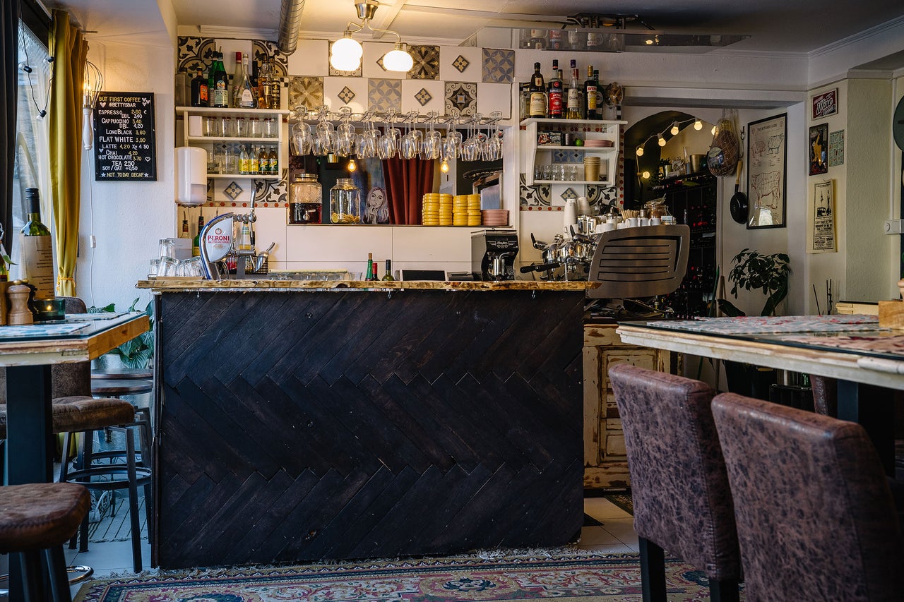 Innenansicht eines Cafés mit Tresen, Regalen und Tischen.