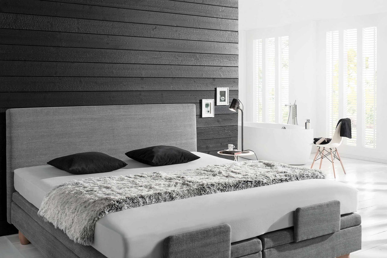 Helles Schlafzimmer mit Boxspringbett, Nachttischlampe und Badewanne