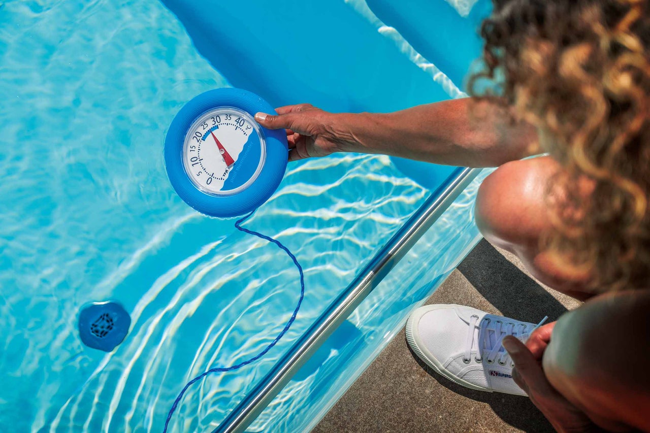 Eine Person misst die Temperatur in einem Pool mit einem Poolthermometer.