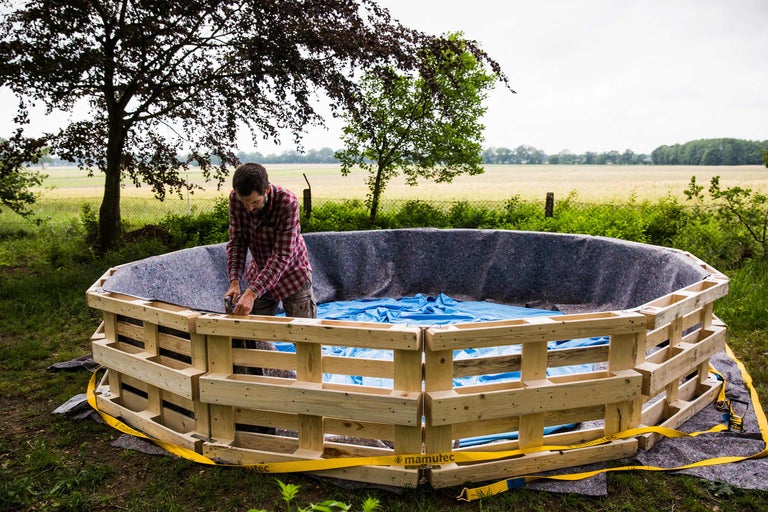 Mann baut einen Pool aus Paletten im Garten, ausgelegt mit Folie und Vlies