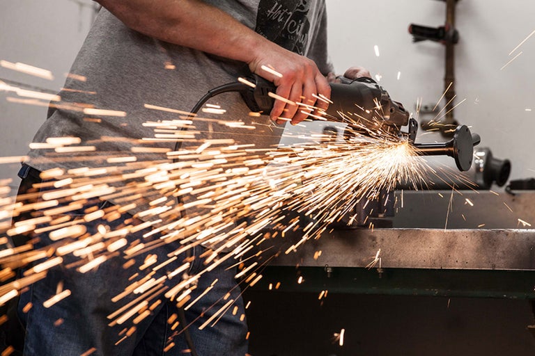 Eine Person schleift mit einer Flex ein Metallstück, Funken sprühen.