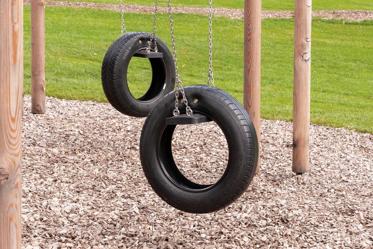 Zwei Reifenschaukeln aus Metallketten und Holzrahmen an Holzpfosten
