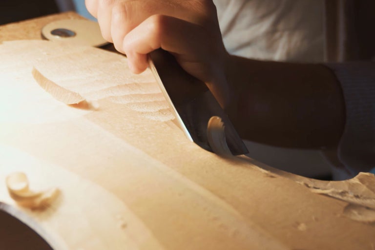 Nahaufnahme einer Person, die mit einem Stecheisen Holz bearbeitet