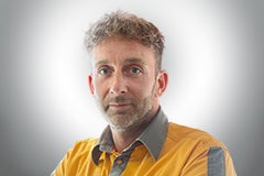 Porträt eines Mannes mit grauem Haar und Bart in gelbem Hemd