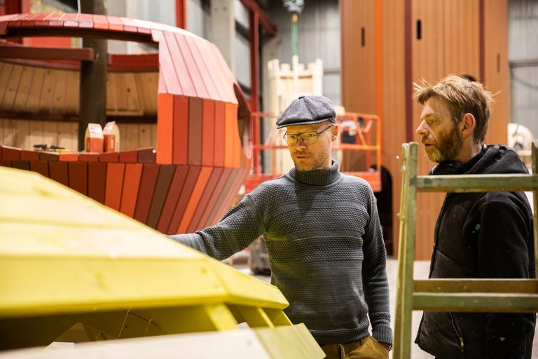 Zwei Männer bei der Arbeit an einer Holzkonstruktion in einer Werkstatt.
