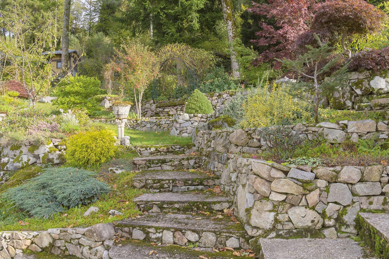 Eine Steintreppe führt durch einen terrassenförmig angelegten Garten mit Steinmauern und verschiedenen Pflanzen