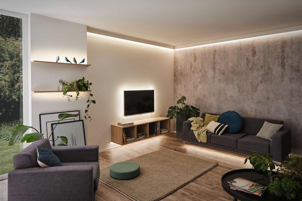 Helles Wohnzimmer mit Sofa, Sessel, Fernseher und Regalen mit Pflanzen und Dekoration