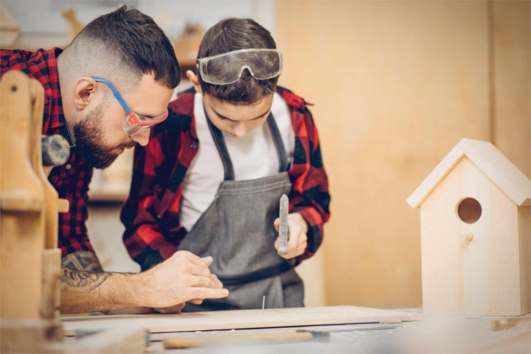Vater und Sohn bauen gemeinsam ein Vogelhaus mit Hammer und Nagel.