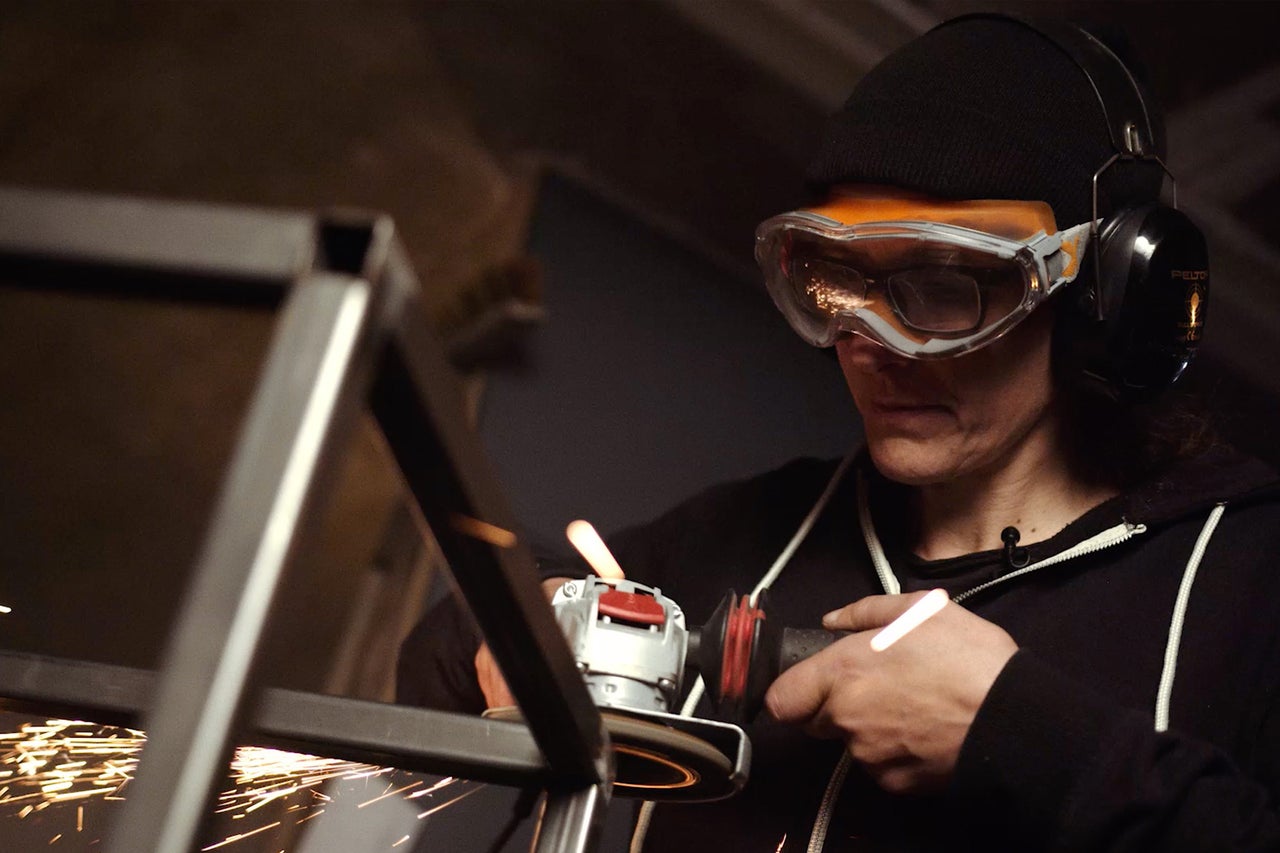 Eine Person schleift Metall mit einer Flex, während Funken sprühen. Sie trägt dabei eine Schutzbrille und Gehörschutz.