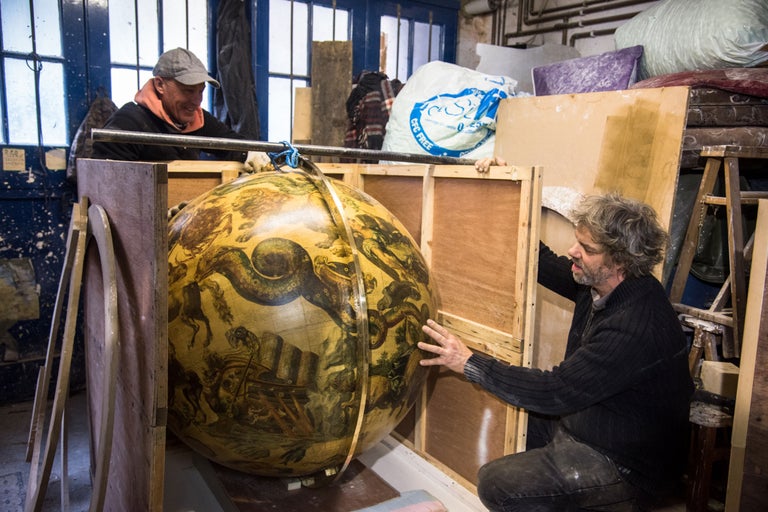 Zwei Personen transportieren einen großen Globus in einer Holzkiste.