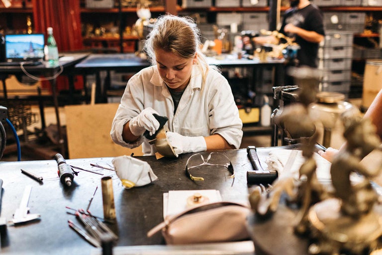 Frau poliert Metallobjekt mit Werkzeugen auf Werkbank