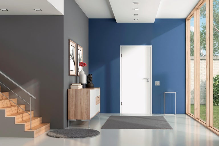 Moderner Eingangsbereich mit weißer Tür vor blauer Wand, Holztreppe, Sideboard und großen Fensterfronten.
