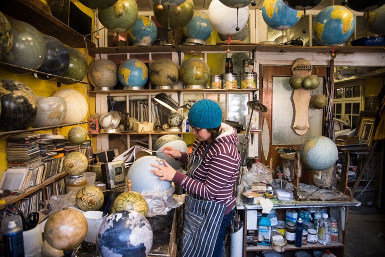 Eine Werkstatt voller Globen, in der eine Person an einem Globus arbeitet